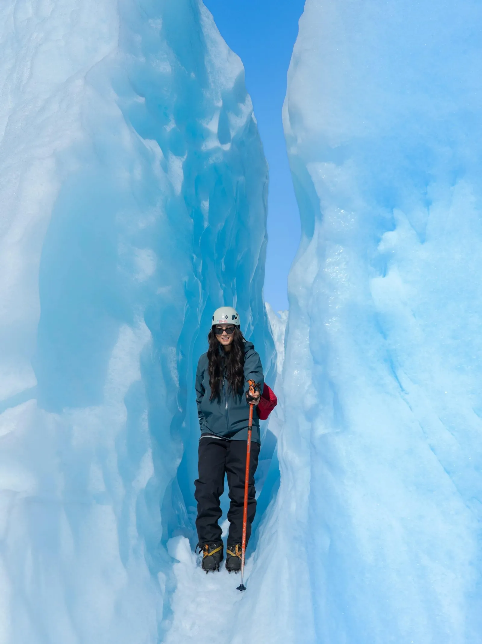 Hiker in helmet standing inside a narrow blue ice crevasse