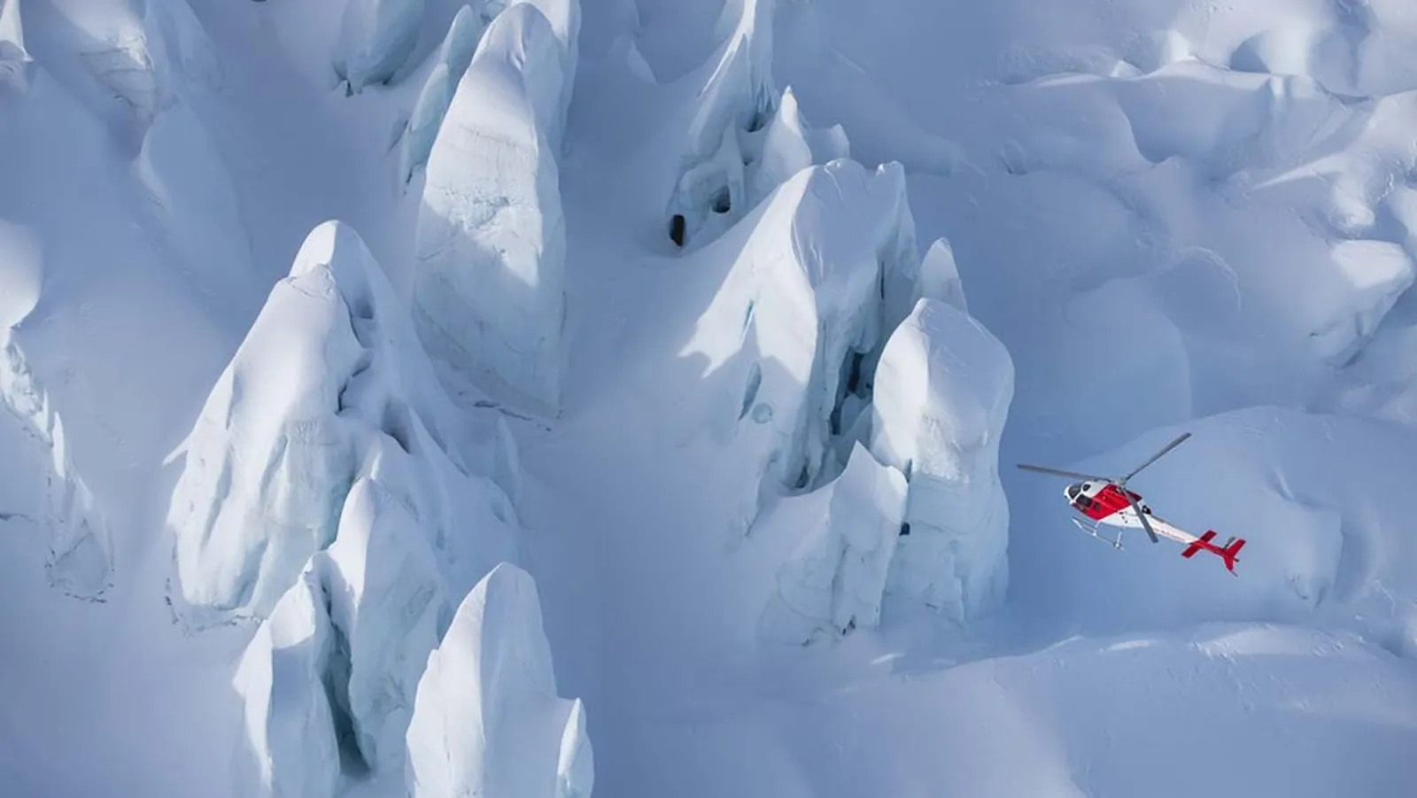 Aerial view of sharp ice pinnacles with a small red helicopter flying above