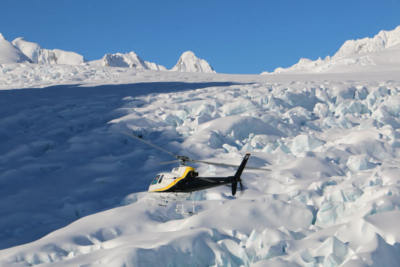 Yellow and black helicopter sitting on a snow-covered glacier with wide mountain horizon