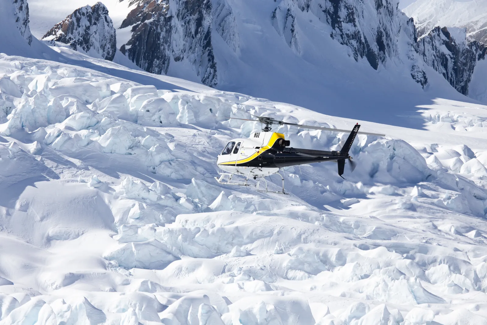 Helicopter descending toward a broken snowfield with jagged mountains in the background
