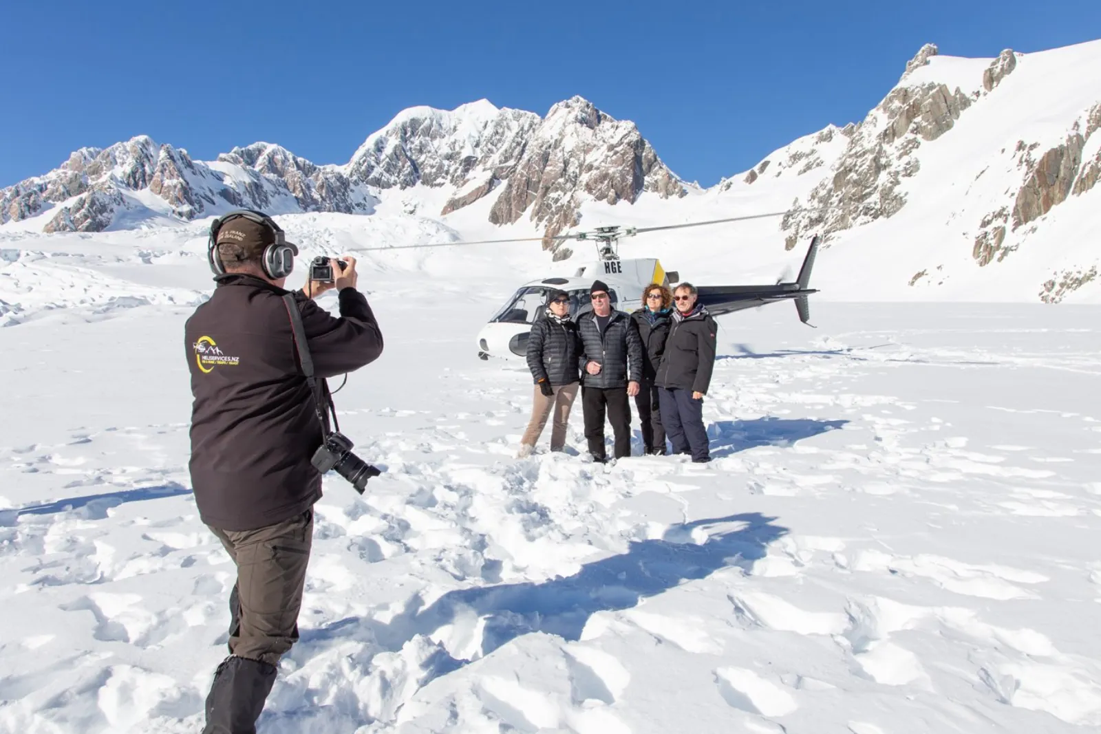 Pilot photographing four passengers beside a helicopter on a sunny snowfield