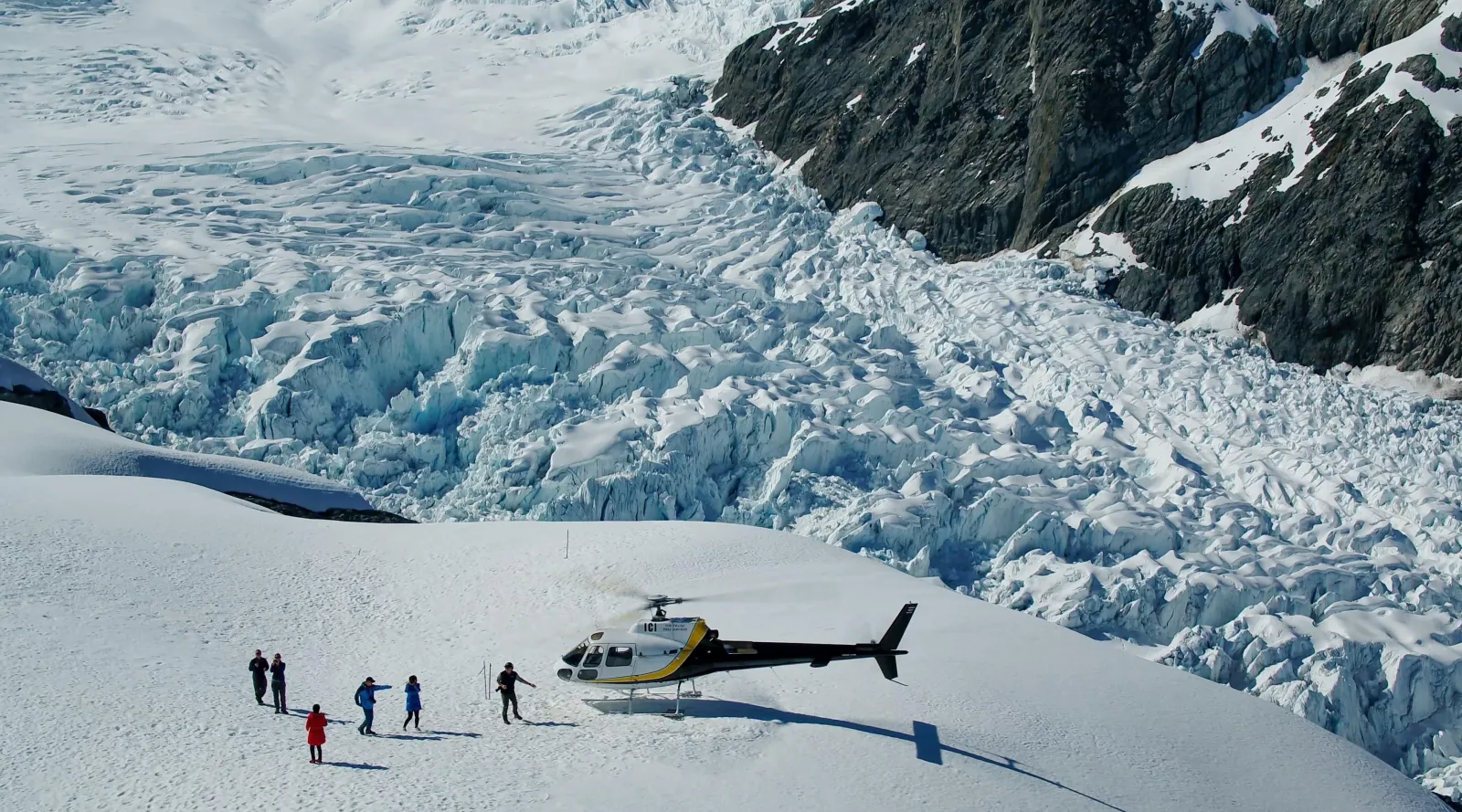 Helicopter landed on snow beside a heavily crevassed icefall with a few people standing near