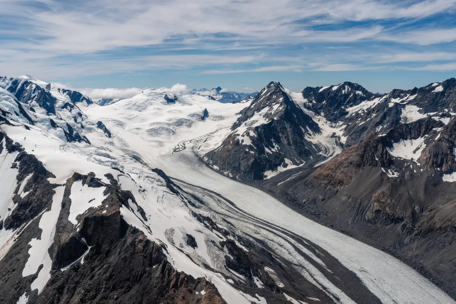 Aerial view of a long glacier winding between dark rocky ridges and snow peaks