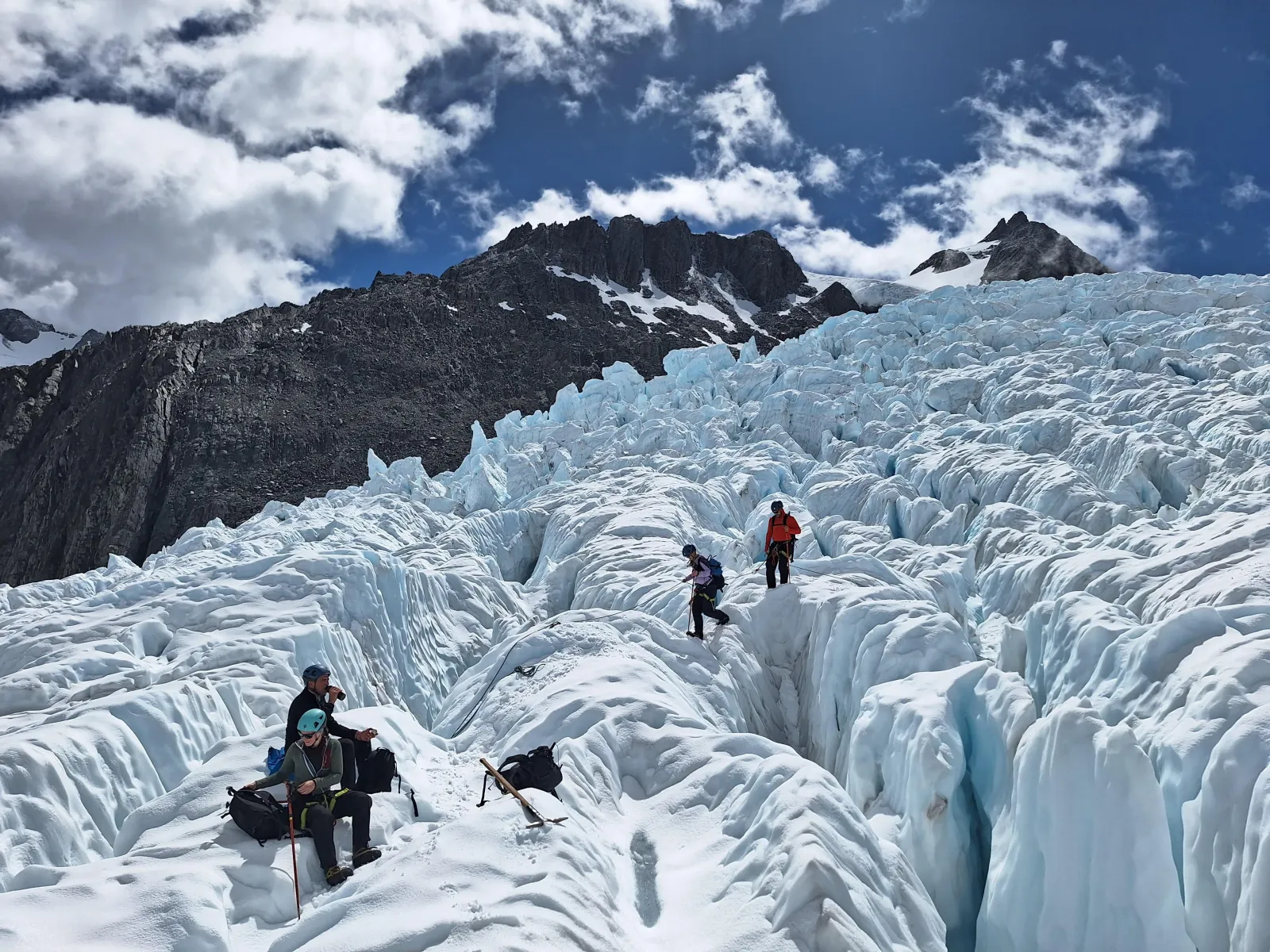 Hikers resting and climbing among crevasses on a glacier with cloud over the ridge